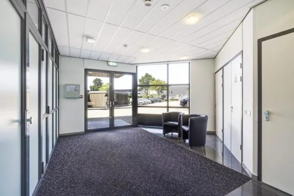 Inkomhal van een bedrijfsgebouw aan de Laan van 's-Gravenmade met glazen entree, zitgedeelte en uitzicht op de parkeerplaats.